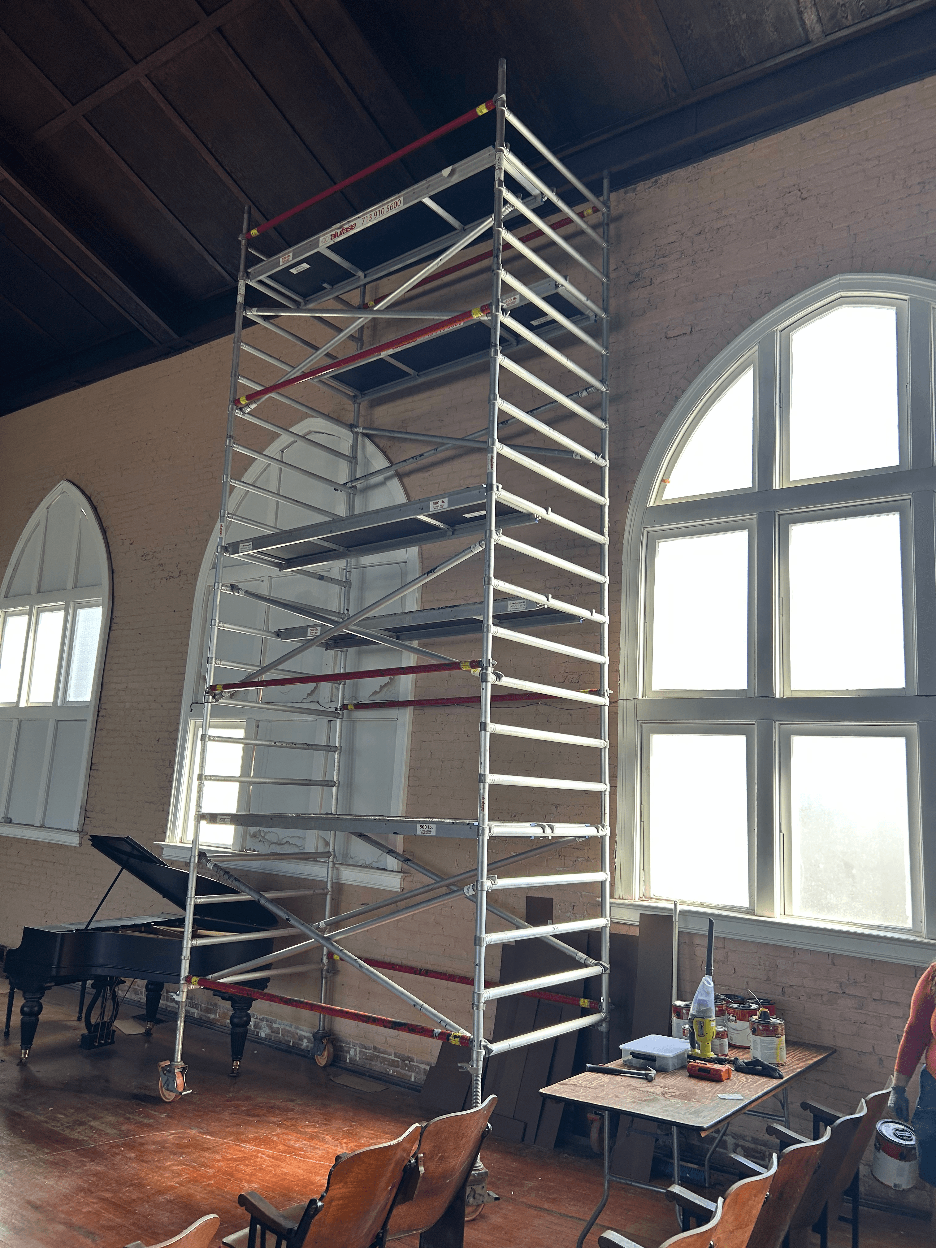 Tall metal scaffolding stands in a room with large arched windows and a grand piano.
