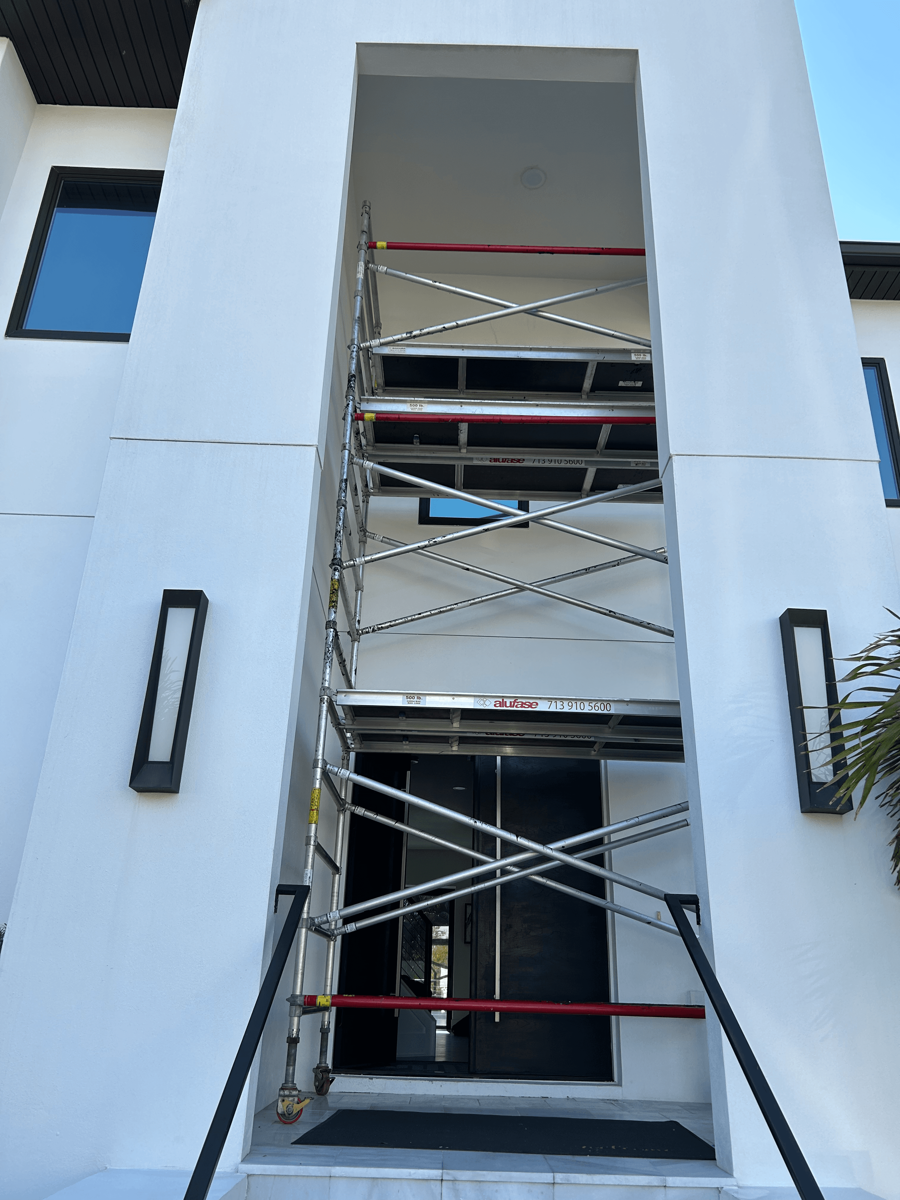 Silver and red metal scaffolding structure erected inside a modern white building's recessed entryway.