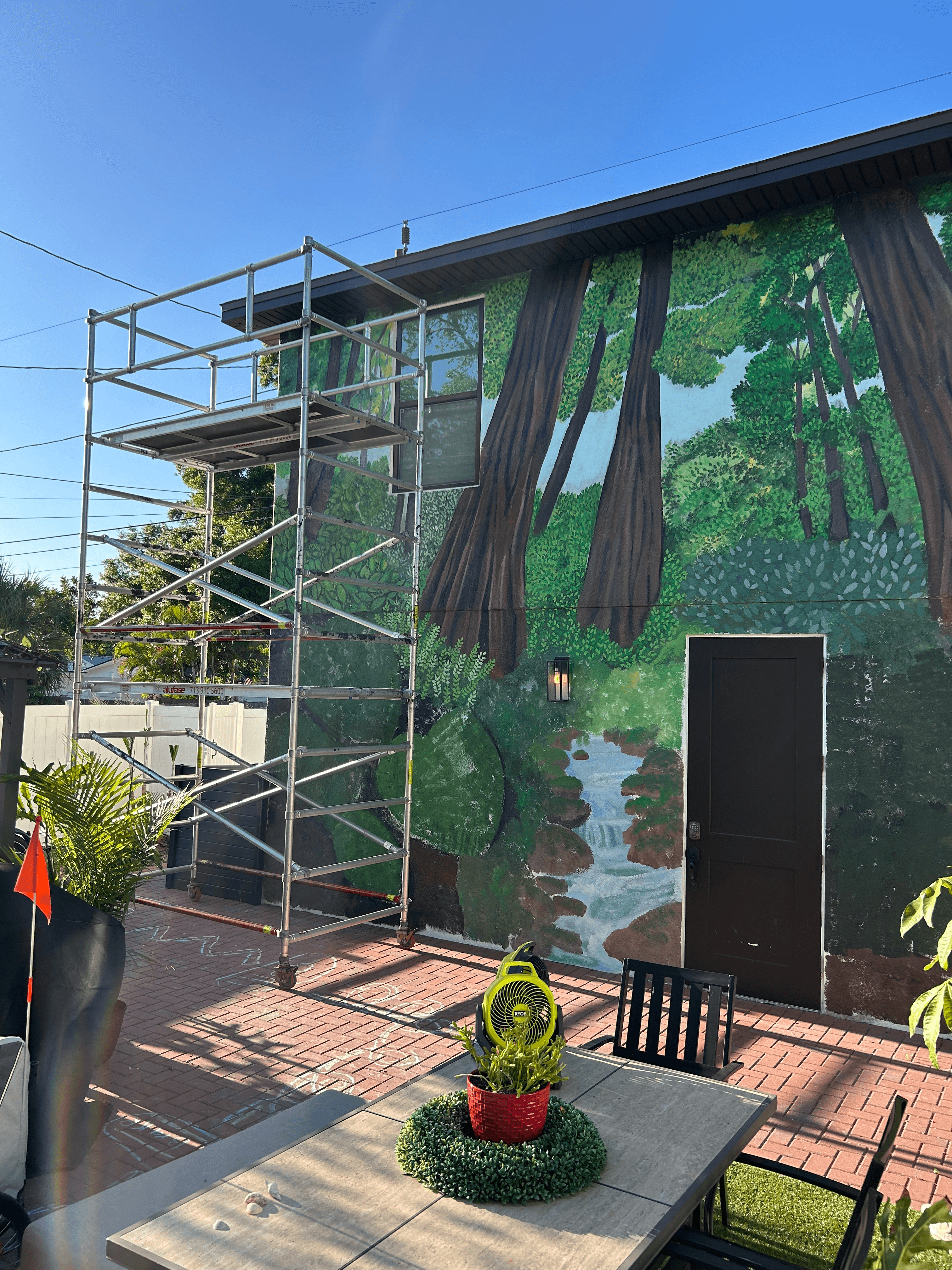Forest mural with tall trees and waterfall on a building wall behind metal scaffolding.
